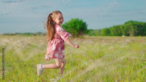 Happy running child in field. Happy family. Little happy girl runs on grass, smiles, in slow motion. Childhood dream concept. Cheerful little girl playing in park in summer. Kid runs across meadow. photo