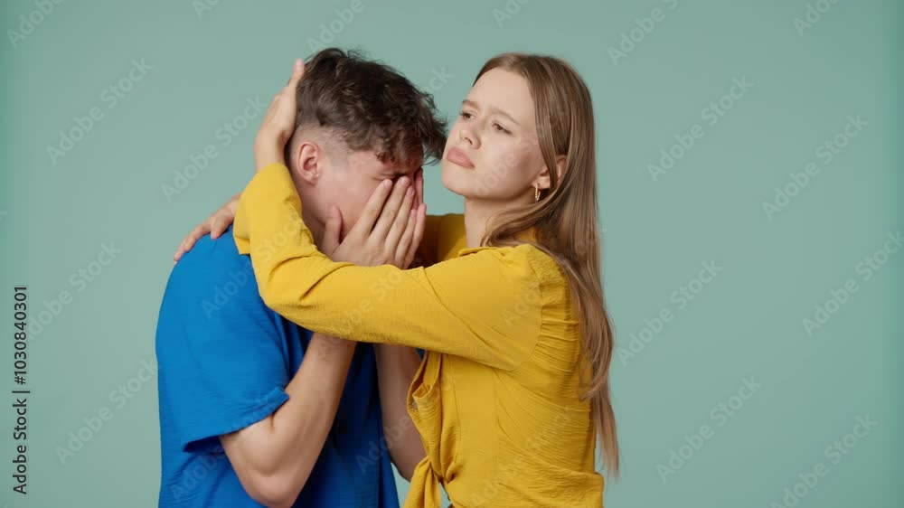 Positive couple of young boyfriend and girlfriend in yellow blue clothes isolated on green background, man is crying woman comforting and hugging him. Positive couple of young boyfriend and girlfriend in yellow blue clothes isolated on green background, man is crying woman comforting and hugging him.