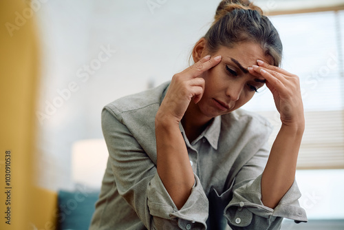 Young distraught woman holding her head in pain at home.