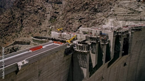 The video shows the ongoing construction of a large dam, featuring significant progress in the structure, with workers and large machinery actively operating on site.