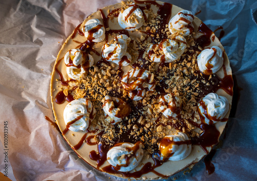 Top view of a decadent dessert featuring whipped cream dollops, drizzled caramel sauce, and crushed nuts on a smooth cake base. The vibrant textures and rich flavors make it a perfect treat.