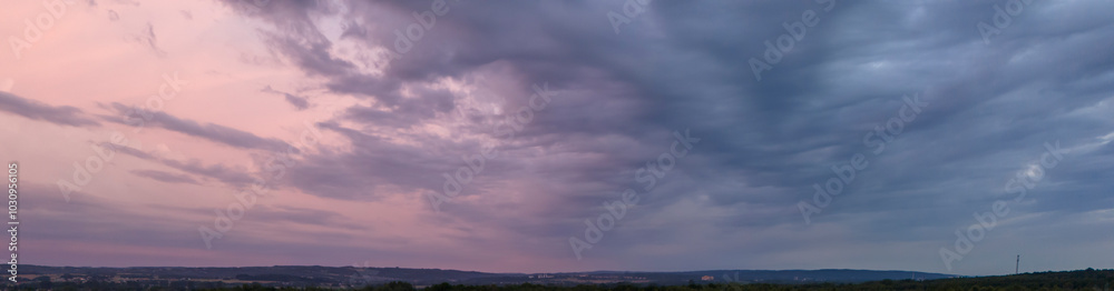A panoramic view of a dramatic sky at dusk with vibrant colors and cloud formations, creating an atmospheric and serene landscape.