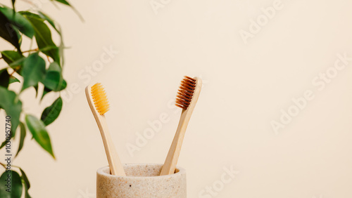 Bamboo toothbrushes in ceramic cup with green leaves and copy space on beige background. Eco friendly organic product, biodegradable and zero waste, minimal aesthetic concept