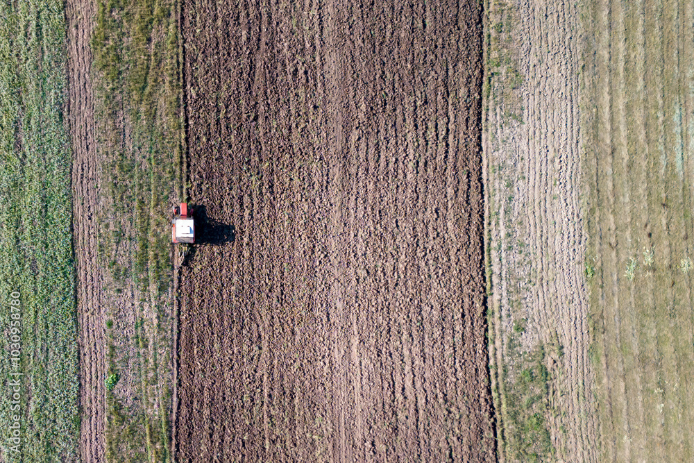 Fototapeta premium Aerial view of a tractor plowing the fields, showcasing agricultural activity and the patterns created on the soil.