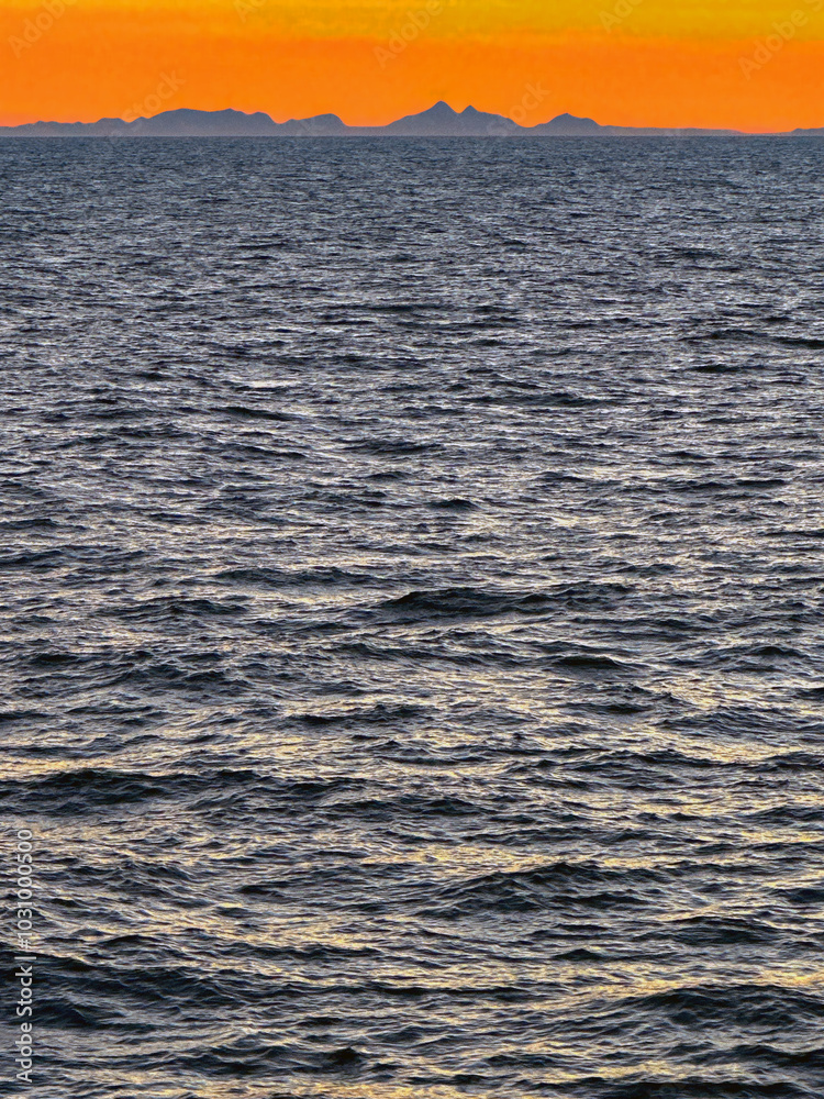 Obraz premium Seascape at sunset with a sihouette of the coast of Greenland on the horizon