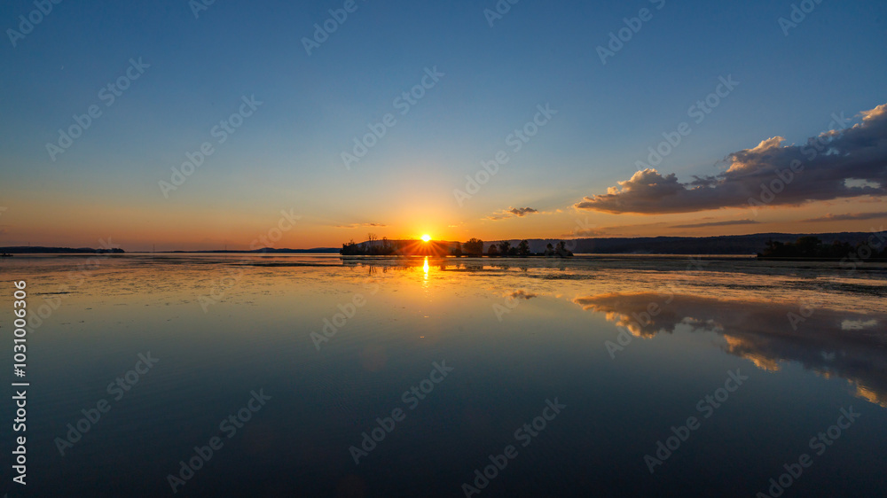 Naklejka premium wide angle view of sunset over a lake with clouds reflected in the water