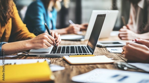 A group of professionals actively engages in brainstorming and planning at a contemporary office. Laptops, notepads, and pens are scattered on the table