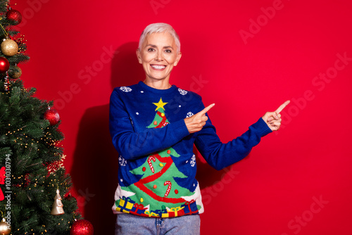 Photo of cheerful glad woman wear ugly print sweater demonstrate empty space isolated on red color background