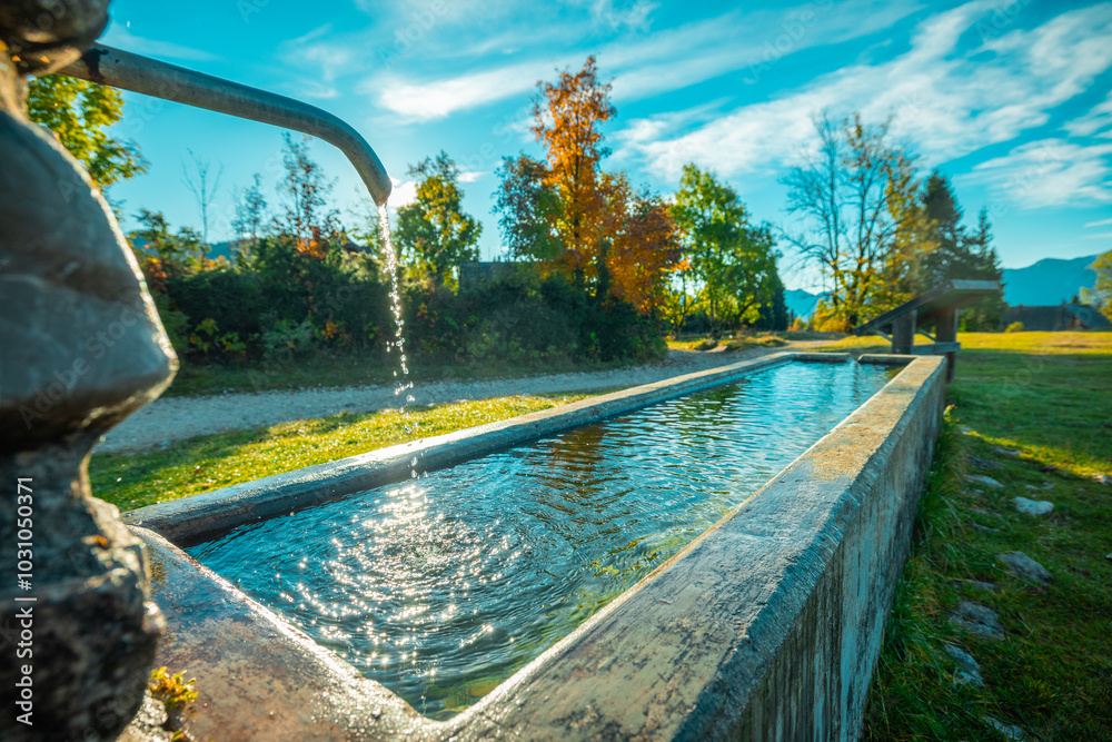 Beautiful water fountain or basin with flowing water on the alpine plain of Uskovnica in slovenian julian alps. Visible sun behind the water tap, flowing into the basin.