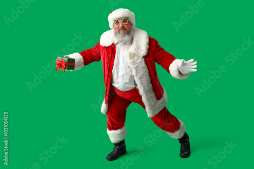 Funny Santa Claus with gift box dancing on green background