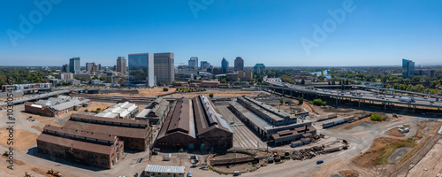 Aerial view of Sacramento, California, featuring historic industrial buildings, modern skyline, Sacramento River, and major highway under a clear blue sky. photo