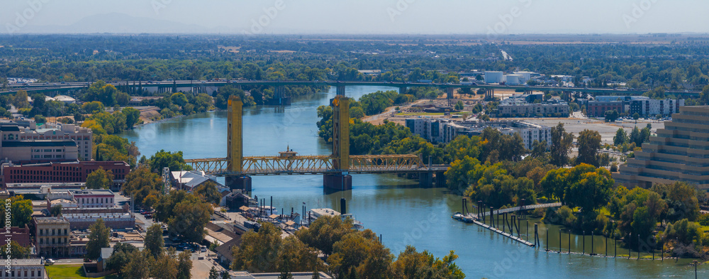 Obraz premium Aerial perspective of Sacramento, California, highlighting the yellow gold Tower Bridge over the Sacramento River, with urban and natural landscapes.