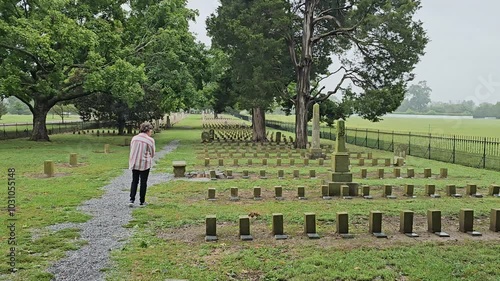 Woman walks respectfully among the Civil War Confederate graves in the McGavock Confederate Cemetery in Franklin, Tennessee on a cold rainy day