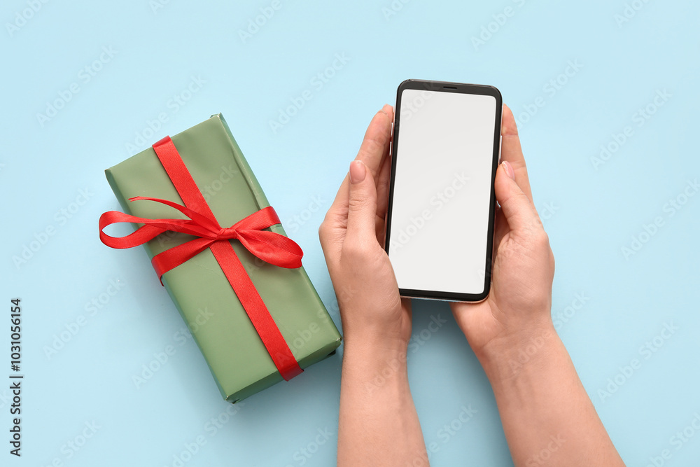 Female hands with mobile phone and Christmas gift box on blue background Female hands with mobile phone and Christmas gift box on blue background