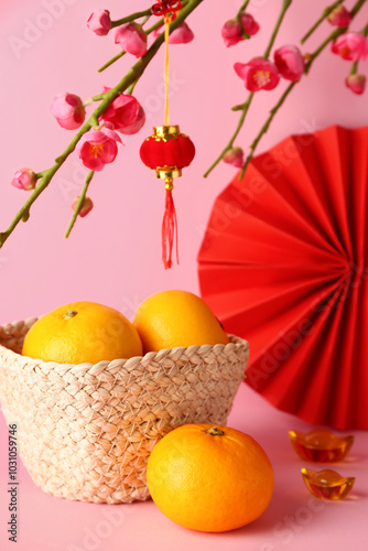 Basket with mandarins, sakura and paper fan on pink background. Japanese New Year celebration photo