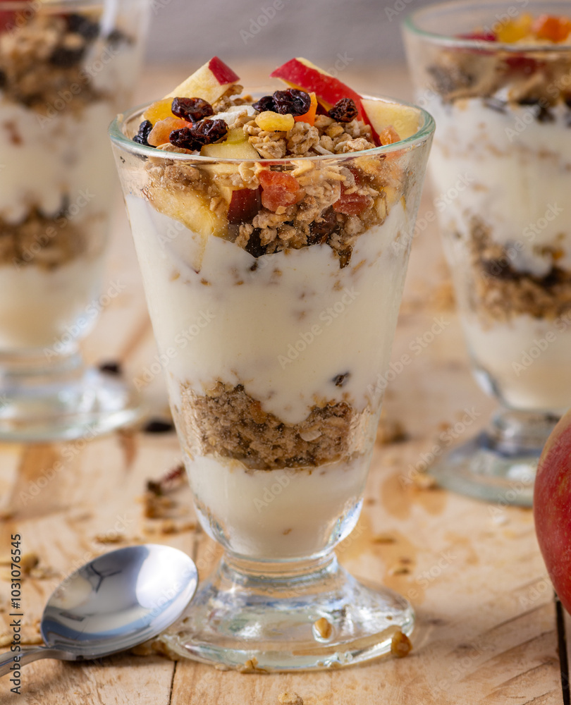 Layered parfait with granola yogurt and fruits in glass cups on wooden table littered with granola Layered parfait with granola yogurt and fruits in glass cups on wooden table littered with granola