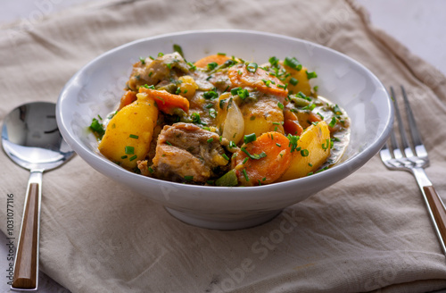 Close up of a bowl of Chicken Potato vegetable soup served on linen fabric with spoon and fork ready to eat