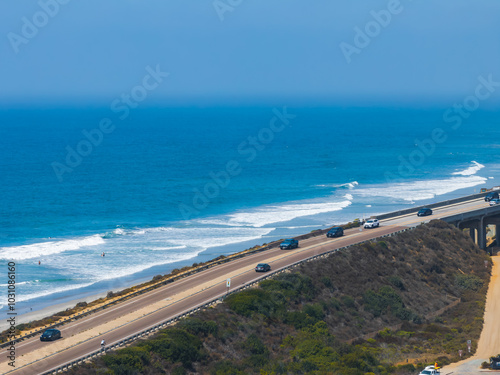 Aerial perspective of a busy coastal highway in San Diego, California, bordered by lush greenery and the expansive Pacific Ocean under a clear sky. photo