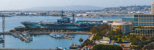 Bild auf Leinwand The image captures an aerial view of the USS Midway Museum in San Diego, California, surrounded by modern buildings, a marina, and rolling hills