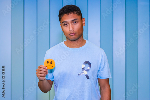 Latino man holding sad face sign with cancer awareness ribbon on t-shirt