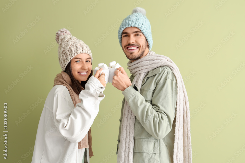 Loving couple in winter clothes with cups of cocoa on green background Loving couple in winter clothes with cups of cocoa on green background