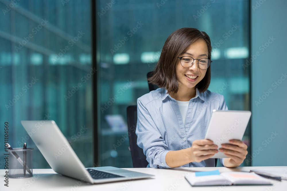 Asian businesswoman using tablet in modern office setting. Positive expression and professional attire suggest productivity and focus. Digital devices enhance idea of connectivity. Asian businesswoman using tablet in modern office setting. Positive expression and professional attire suggest productivity and focus. Digital devices enhance idea of connectivity.