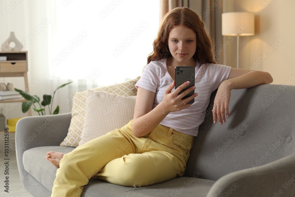 Obraz premium Beautiful teenage girl using smartphone on sofa at home