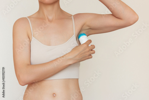 Portrait of young woman in beige underwear applying a ball deodorant to her armpits. Hygiene and body care. Preventing the smell of sweat.