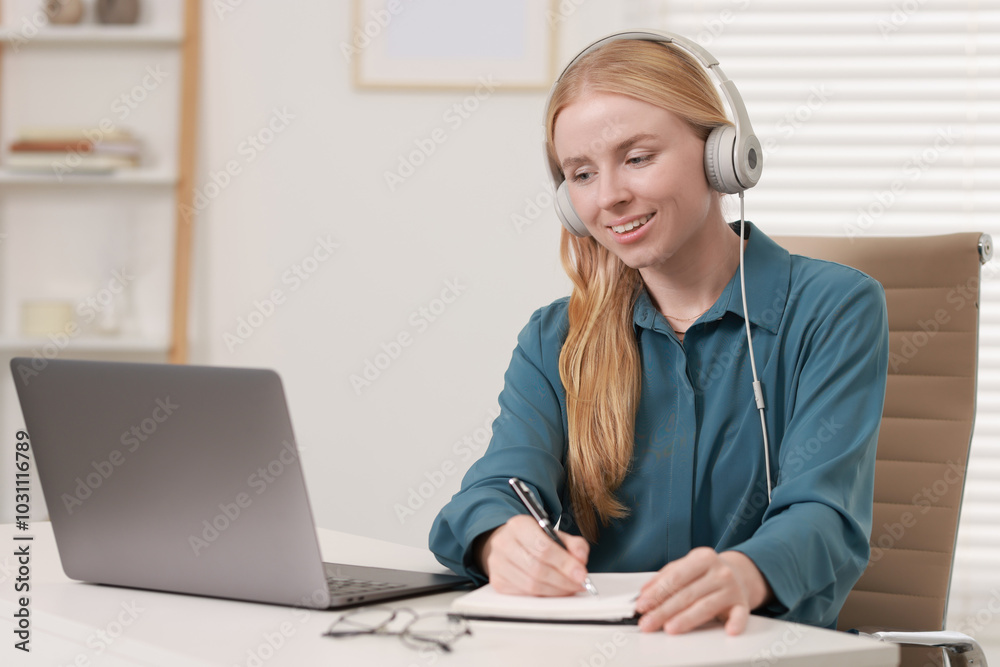 Interpreter in headphones taking notes while working with laptop at table indoors Interpreter in headphones taking notes while working with laptop at table indoors
