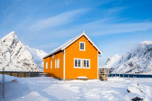 Traditional yellow rorbu house and Olstind mountain peak in Sakrisoy fishing village on Lofoten islands, Norway. Winter landscape with snowy mountains and Scandinavian cottage photo