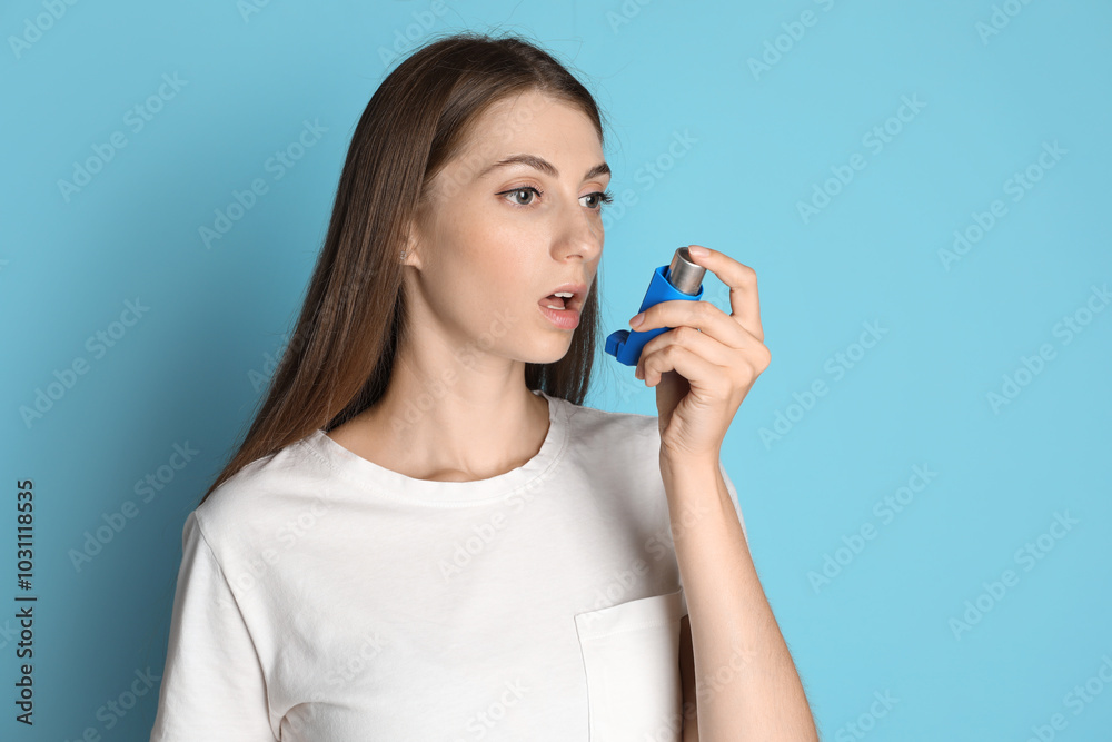 Young woman using asthma inhaler on light blue background Young woman using asthma inhaler on light blue background