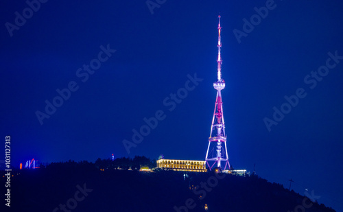 Obraz na płótnie Illuminated Tbilisi TV tower at night showcasing colorful lights on a clear evening in the cityscape. A TV tower stands against the night sky in the capital of Georgia creating a vibrant display. w salonie