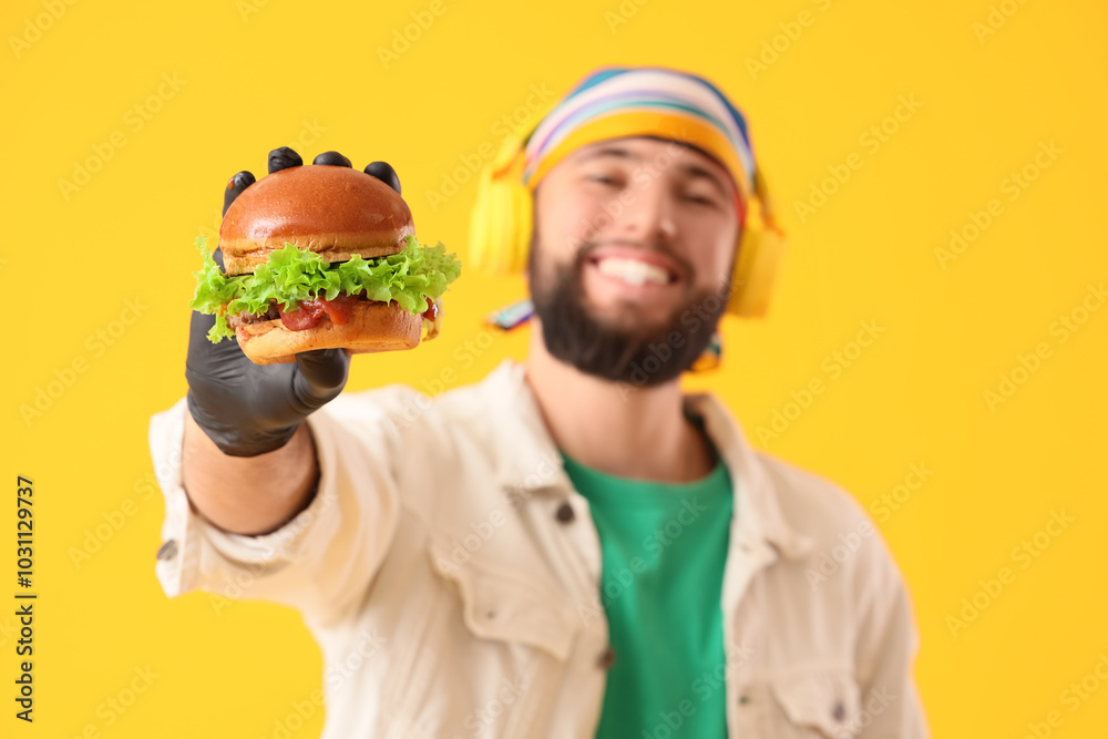 Young man in black glove holding tasty burger on yellow background Young man in black glove holding tasty burger on yellow background