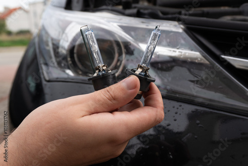 Obraz na plátne A man's hand holds two xenon bulbs against the blurred background of a car headlight