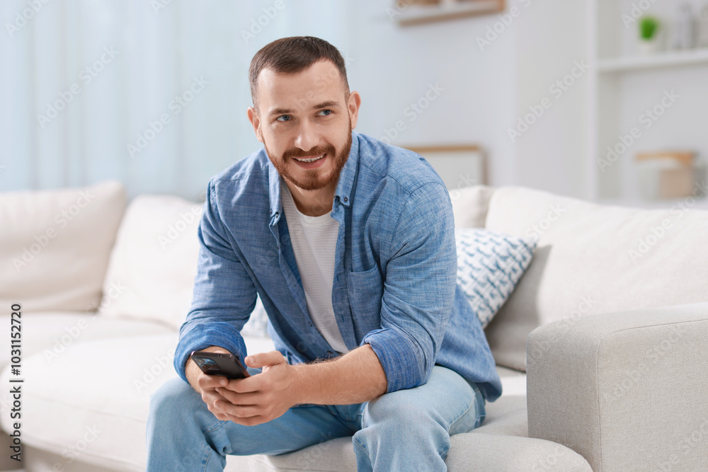 Smiling man with smartphone on sofa at home Smiling man with smartphone on sofa at home