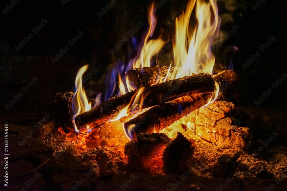 Campfire with yellow and blue flames above glowing bed of orange and white ashes and embers in landscape orientation Campfire with yellow and blue flames above glowing bed of orange and white ashes and embers in landscape orientation