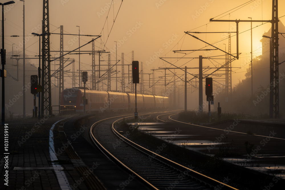 The train platform glows softly in the morning light, with dawn's golden hue wrapped in mist. A red train slowly arrives, ready for the early crowd. The train platform glows softly in the morning light, with dawn's golden hue wrapped in mist. A red train slowly arrives, ready for the early crowd.