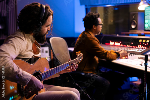 Musician composing new tracks on his electro acoustic guitar, playing record on instrument to create an album. Singer collaborating with producer to make new records in control room at studio.