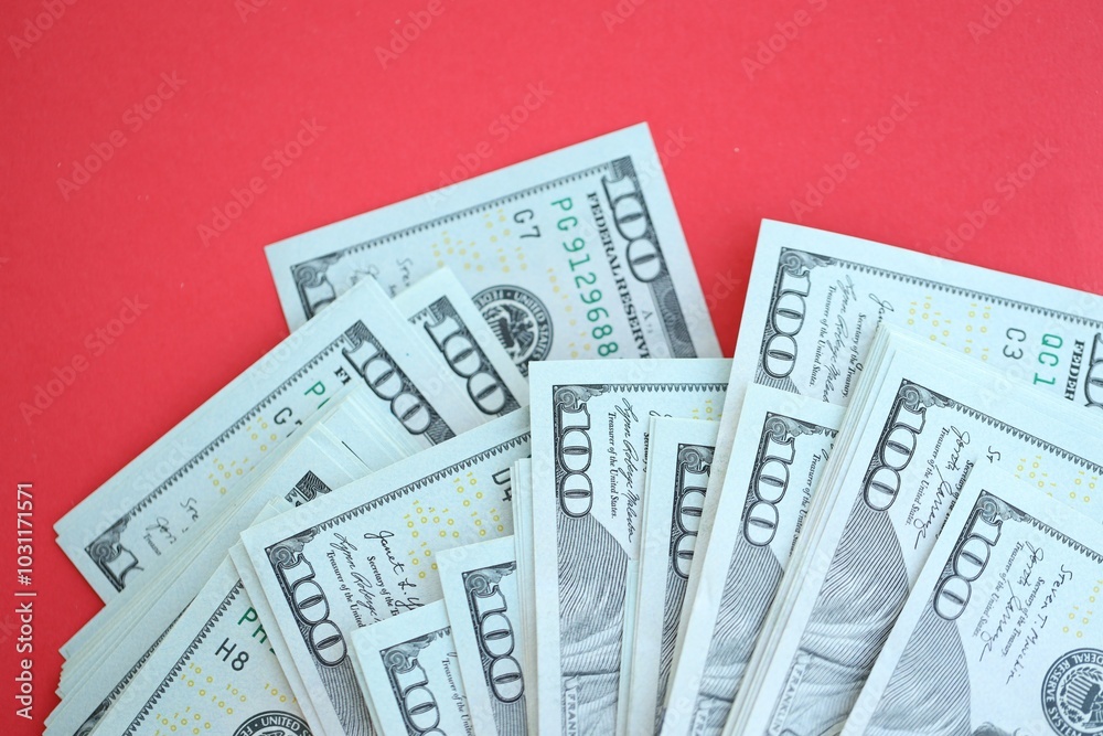 Big amount of hundred dollar bills in thick stack lies on bright red color paper background Big amount of hundred dollar bills in thick stack lies on bright red color paper background