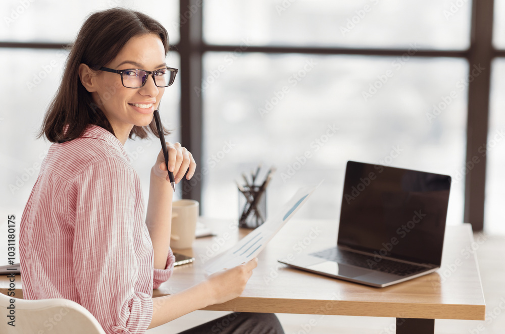 Over the Shoulder. Female Analyst Holding Paper With Statistics, Graphs and Charts Sitting at Desk in Creative Office Over the Shoulder. Female Analyst Holding Paper With Statistics, Graphs and Charts Sitting at Desk in Creative Office