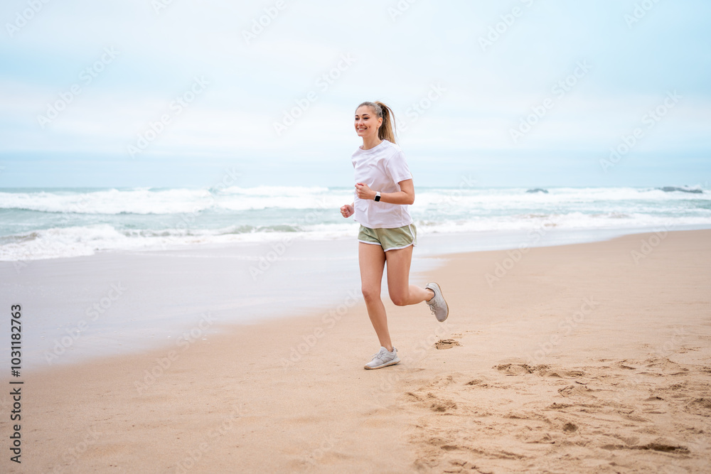 Happy sporty woman jogging on wet seashore against sky at beach. Full body of smiling female is looking away while exercising during daytime. Happy sporty woman jogging on wet seashore against sky at beach. Full body of smiling female is looking away while exercising during daytime.