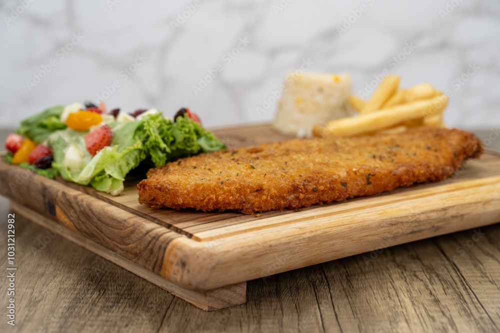 Breaded fish fillet arranged on a wooden platter and served with french fries and salad for a delicious seafood meal Breaded fish fillet arranged on a wooden platter and served with french fries and salad for a delicious seafood meal