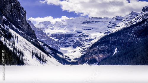 Early May 2024, Lake Louise was still frozen and many people wandered onto the lake. The lake's snow covered surface is surrounded by snow-covered forests and mountains.