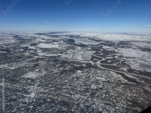 Snow-covered ground near Des Moines, Iowa, seen from an airplane window.A frozen river, lake and a snow-covered cityscape.