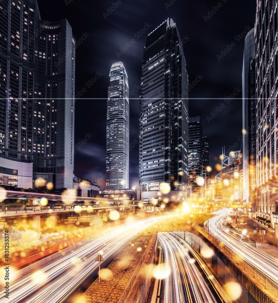 Obraz premium Nighttime view of Hong Kong's cityscape, showcasing towering skyscrapers illuminated with lights against a dark sky. A bustling freeway with bright streaks of light from moving cars can be seen below