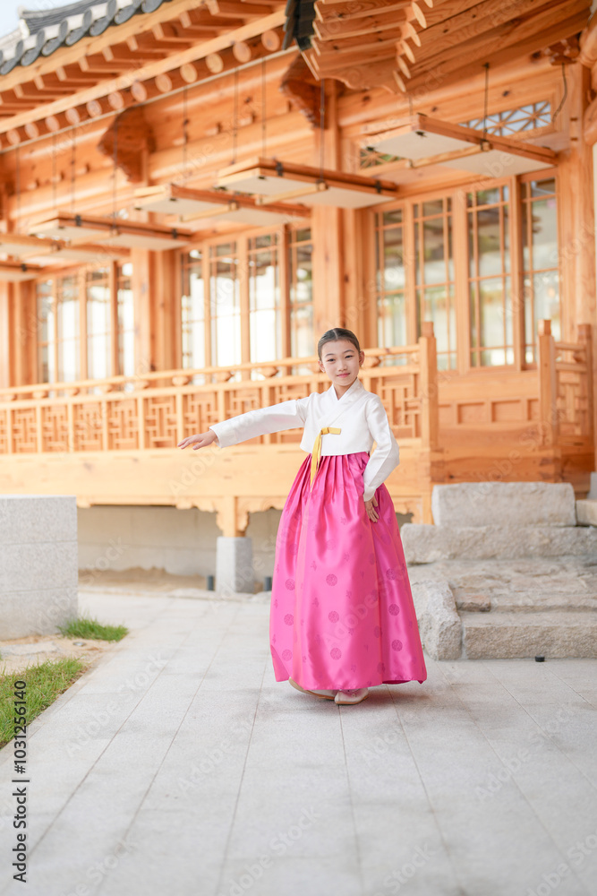 Obraz premium A 9-year-old Korean girl wearing a hanbok is performing a traditional dance in front of a traditional building in the historic town of Gyedong-gil, Jongno District, Seoul, Korea.