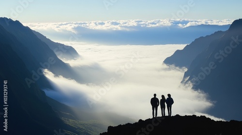 Three people stand silhouetted against a breathtaking sunrise over a valley filled with clouds.