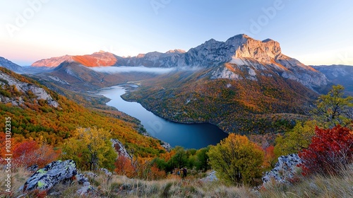 A breathtaking landscape featuring a stunning mountain range shrouded in mist, with a winding river below. Captured during golden hour, the warm light enhances the vibrant colors of the foliage. In