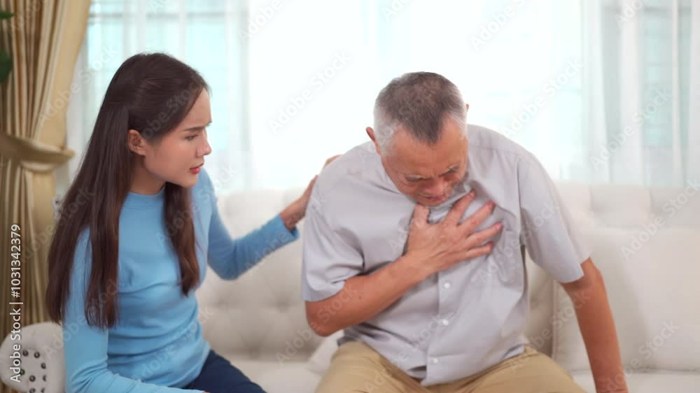 elderly Asian man is sitting on a sofa in the living room with his daughter. Then, the man gets up and experiences severe chest pain due to a disease. elderly Asian man is sitting on a sofa in the living room with his daughter. Then, the man gets up and experiences severe chest pain due to a disease.
