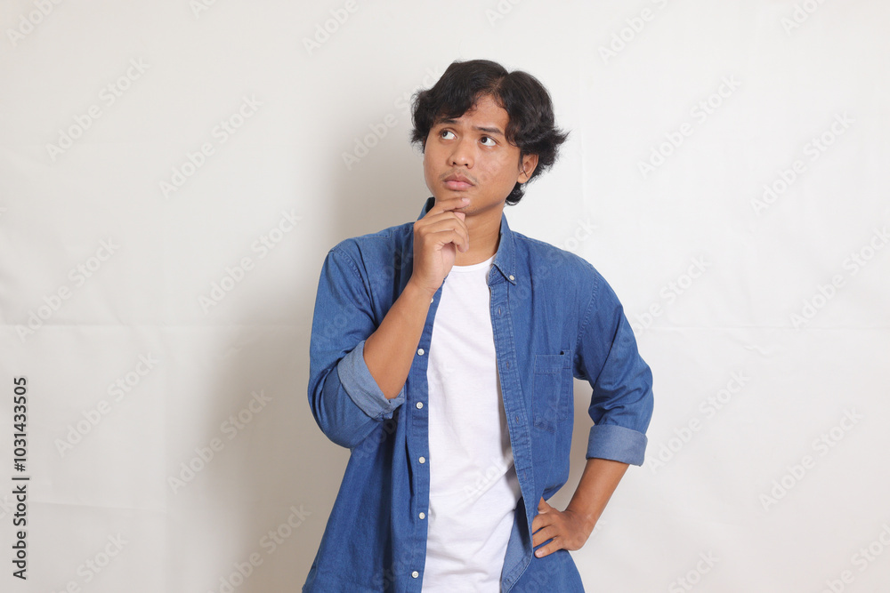 Portrait of confused Asian man in blue shirt thinking about question with hand on chin. Isolated image on white background Portrait of confused Asian man in blue shirt thinking about question with hand on chin. Isolated image on white background